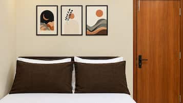 A bedroom with a bed, a wooden door, and three framed artworks on the wall.