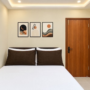 A bedroom with a bed, a wooden door, and three framed artworks on the wall. - Hotel The Pavilion (Tadepalle)