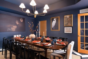 A dining area with a long table set for six, surrounded by chairs, with a vase of branches and candles on the table. - Luxe Cabin •Sauna•Hot Tub•Theater•Arcade•6 Kings (Galena)