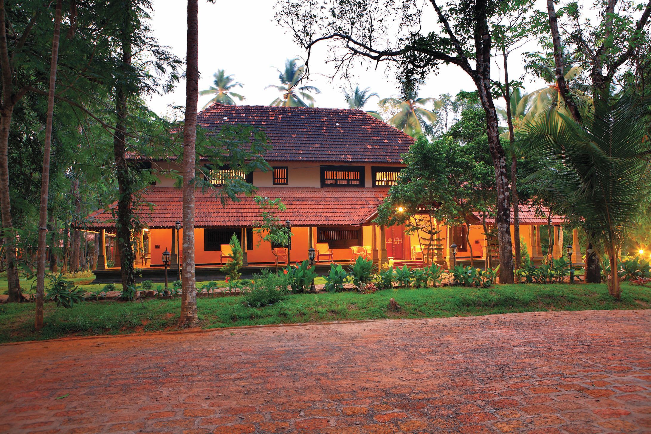 A traditional house with a tiled roof, surrounded by lush greenery and palm trees.
