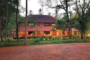 A traditional house with a tiled roof, surrounded by lush greenery and palm trees.