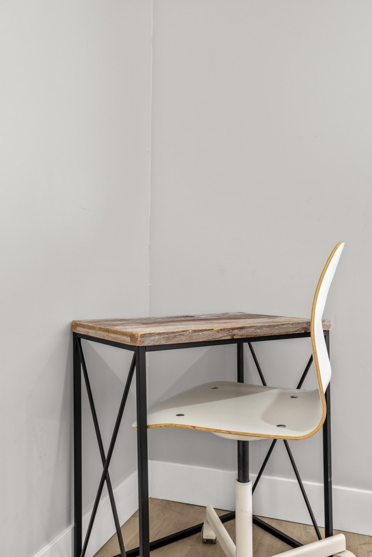 Una mesa en esquina con tapa de madera y estructura metálica negra, acompañada por una silla blanca con respaldo curvo.