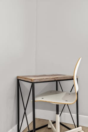 Una mesa en esquina con tapa de madera y estructura metálica negra, acompañada por una silla blanca con respaldo curvo.