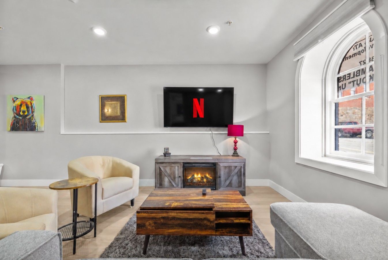 Una sala de estar moderna con chimenea, televisor montado en la pared y ventana con vistas a la calle.
