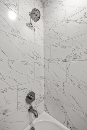 A bathroom with white marble tiles, a showerhead, and a bathtub.