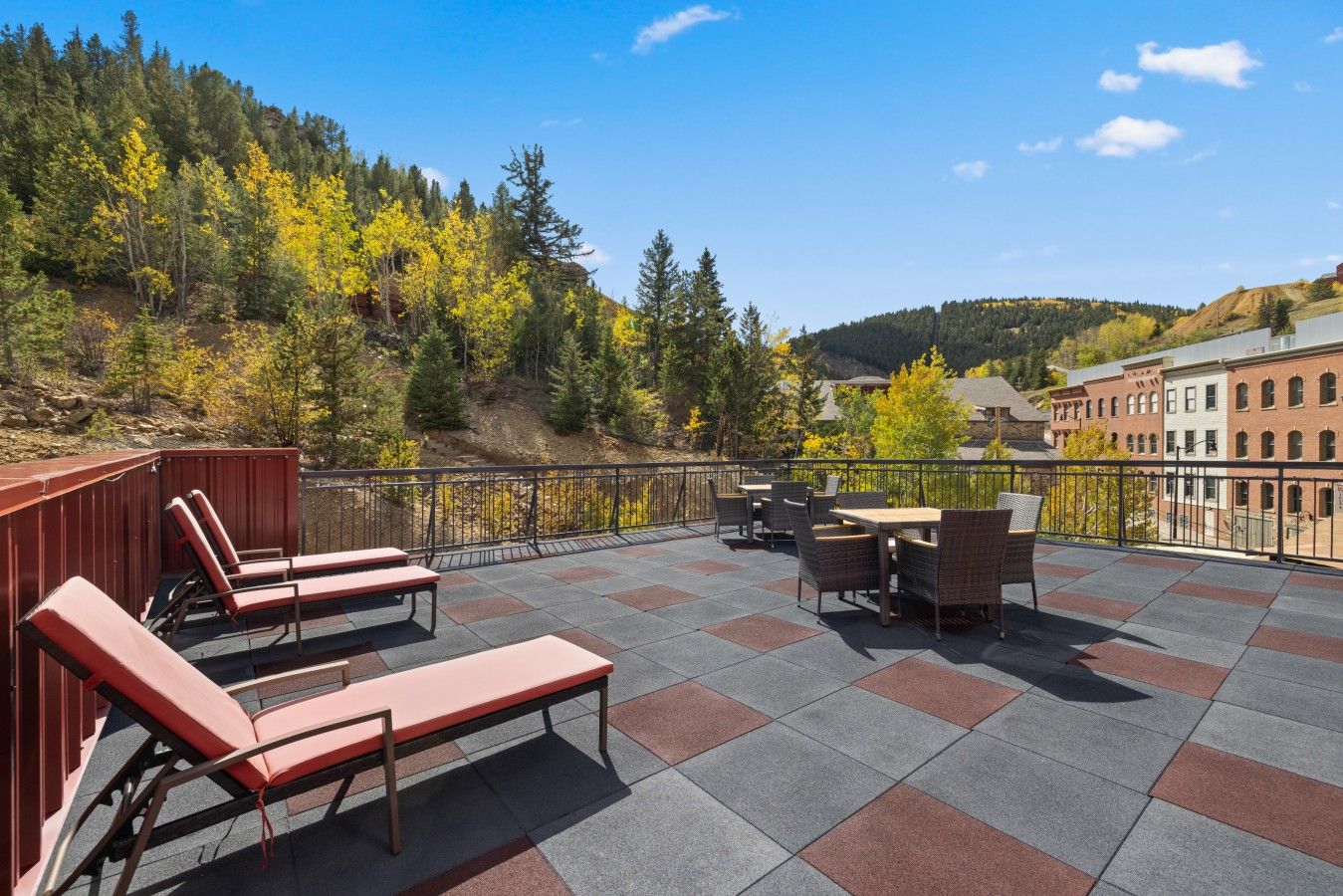 Una terraza con asientos al aire libre, vista a una ladera boscosa y edificios al fondo.