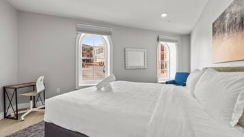 Un dormitorio con una cama grande, dos ventanas, un escritorio y una silla.
