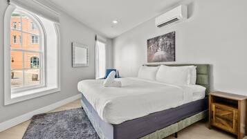 Un dormitorio moderno con una cama grande, una mesita de noche, un ventanal y un equipo de aire acondicionado.