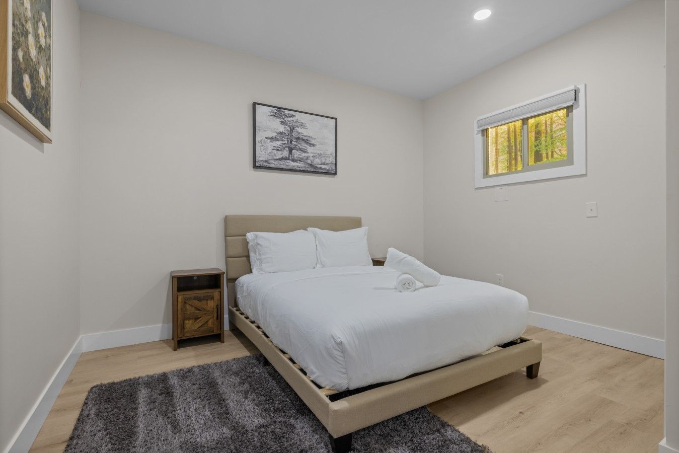 Un dormitorio con cama, mesita de noche, ventana con vistas y un cuadro en la pared.