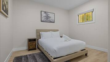 Un dormitorio con cama, mesita de noche, ventana con vistas y un cuadro en la pared.