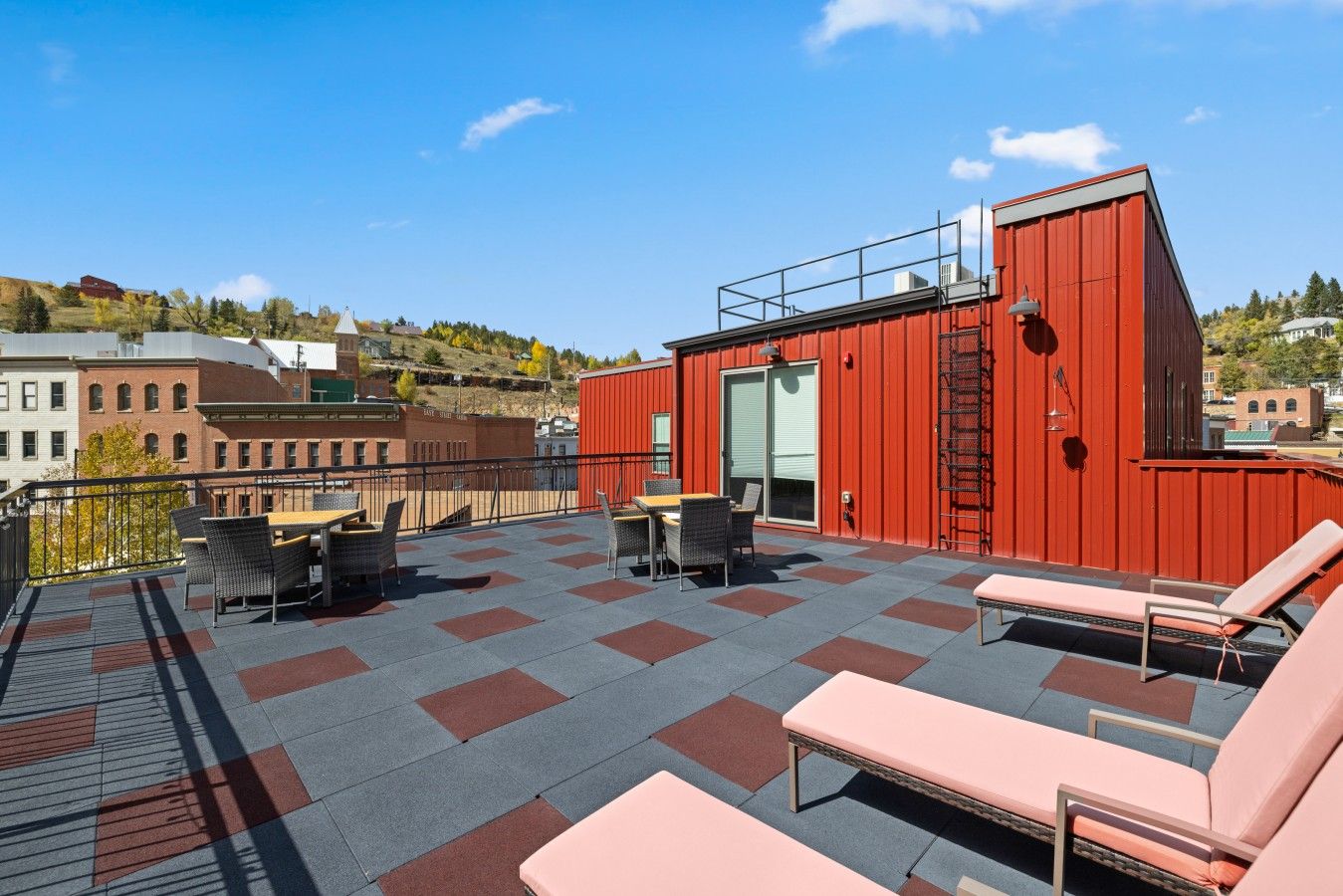 Een terras op het dak met buitenmeubilair, een rood gebouw en een stadsgezicht.