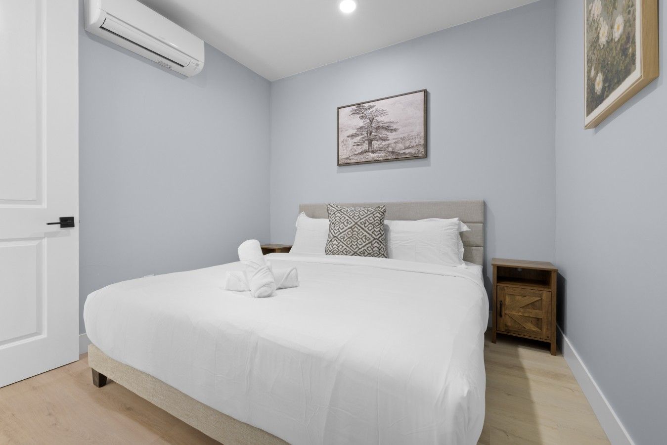 Een slaapkamer met een bed, nachtkastje, een luchtverkoeler aan de muur en een ingelijste foto.