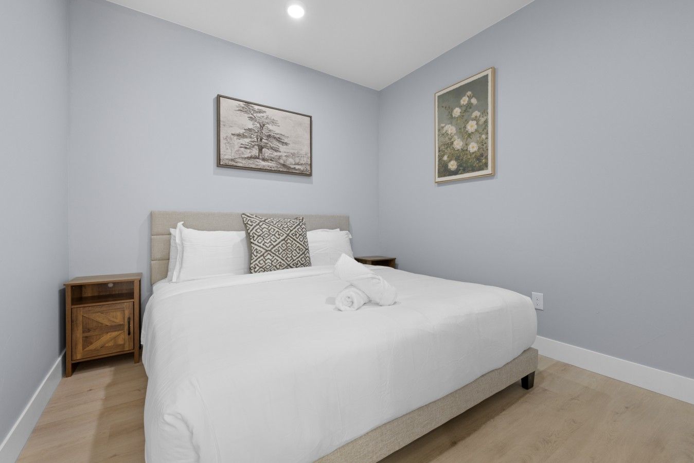 Un dormitorio con una cama, dos mesitas de noche, un armario de madera y dos cuadros en la pared.