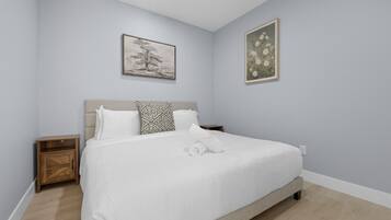 Un dormitorio con una cama, dos mesitas de noche, un armario de madera y dos cuadros en la pared.