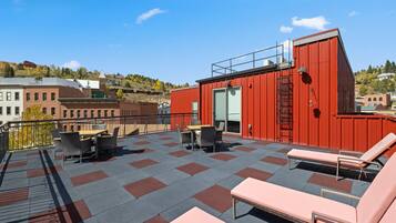 A rooftop terrace with outdoor seating, a red building, and a cityscape view.