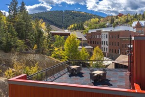 Una terraza en la azotea con mobiliario exterior, con vistas a un pueblo con edificios y montañas al fondo.
