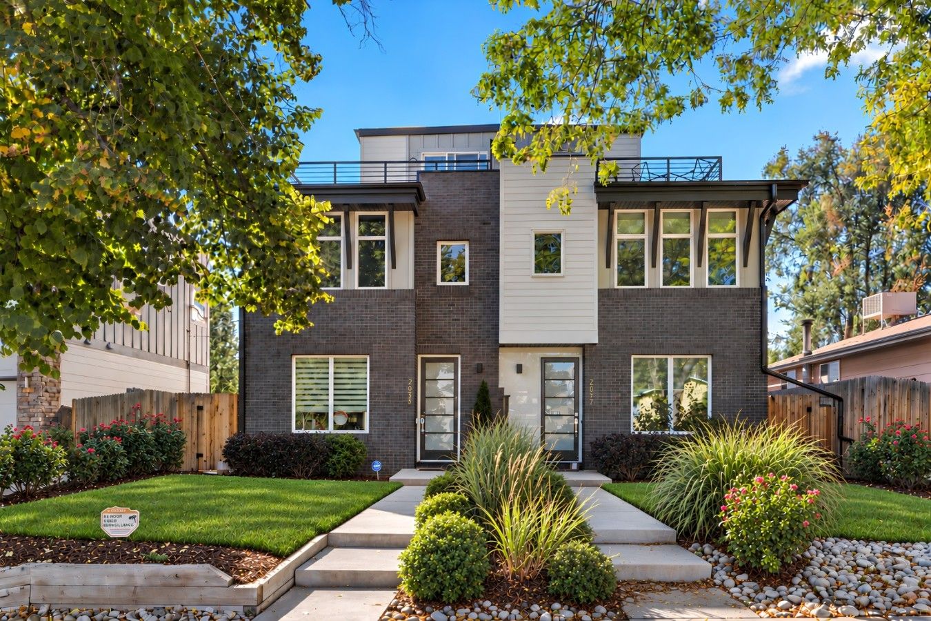 A modern two-story house with a brick facade, large windows, and a well-maintained front yard with a pathway leading to the entrance.