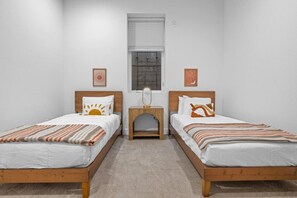 A room with two wooden beds, a small wooden nightstand, a window with blinds, and two wall-mounted artworks. - Denver Designer Retreat | Hot Tub | Rooftop Decks (Denver)