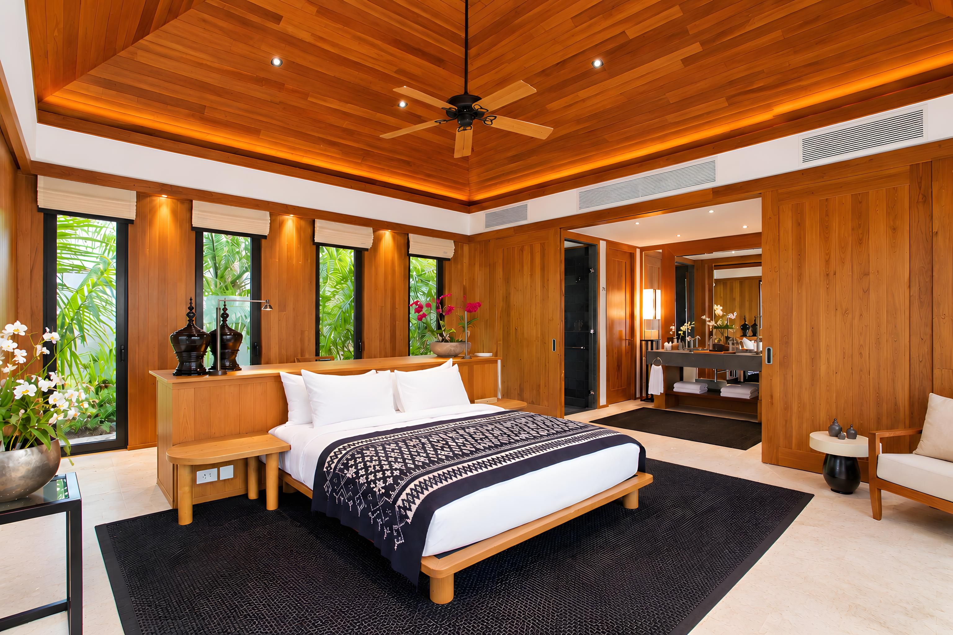 A modern bedroom with a large bed, wooden ceiling, and a view of greenery outside.