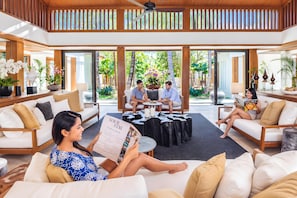 A spacious living area with a high ceiling, large windows, and a view of a lush garden. There are multiple seating areas with sofas and a coffee table. - Villa Nandana 7BR/Beachfront/Gym/Maid/BF (Takua Thung)