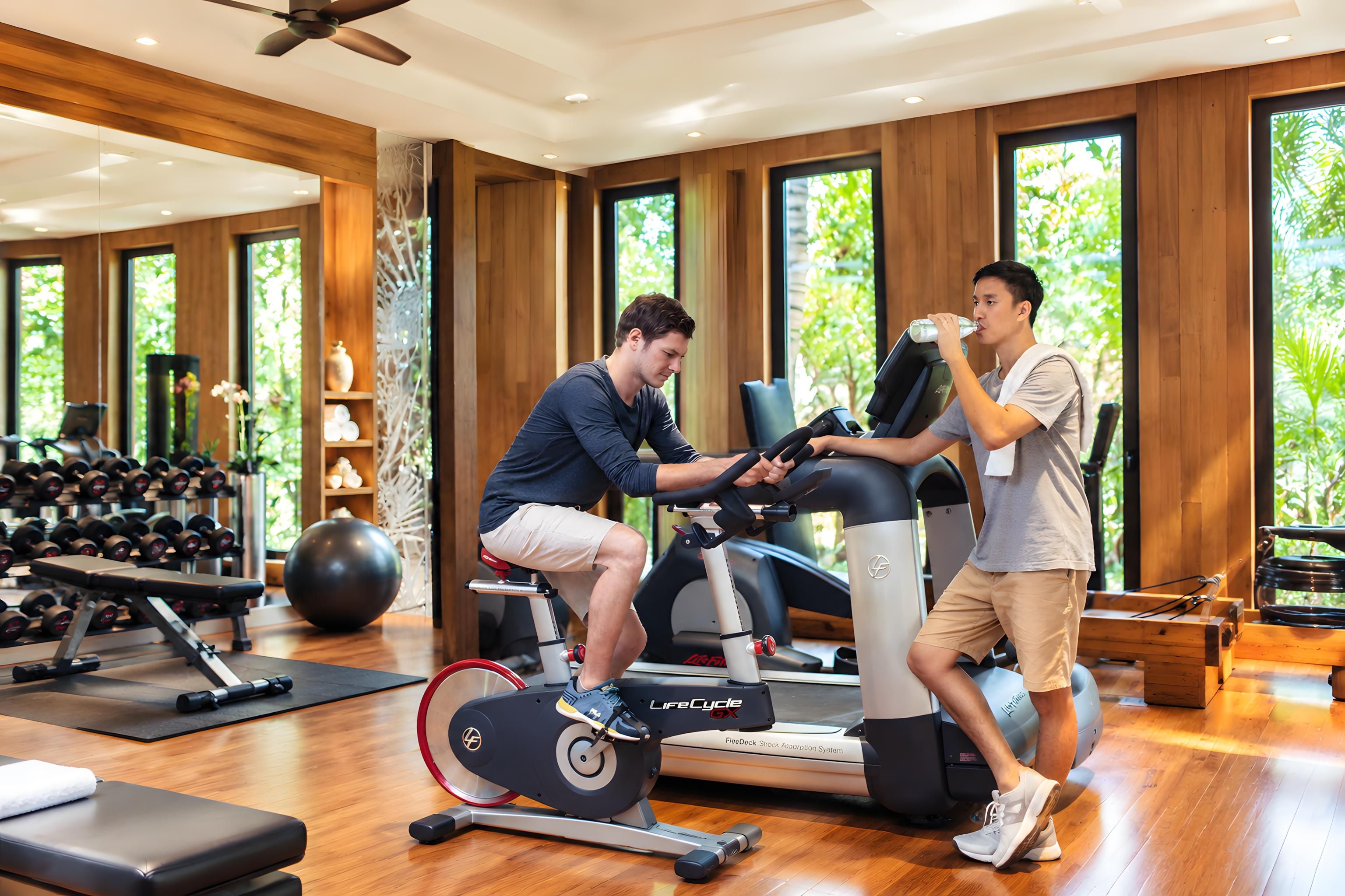 A gym with exercise equipment, a treadmill, and a person using a stationary bike.