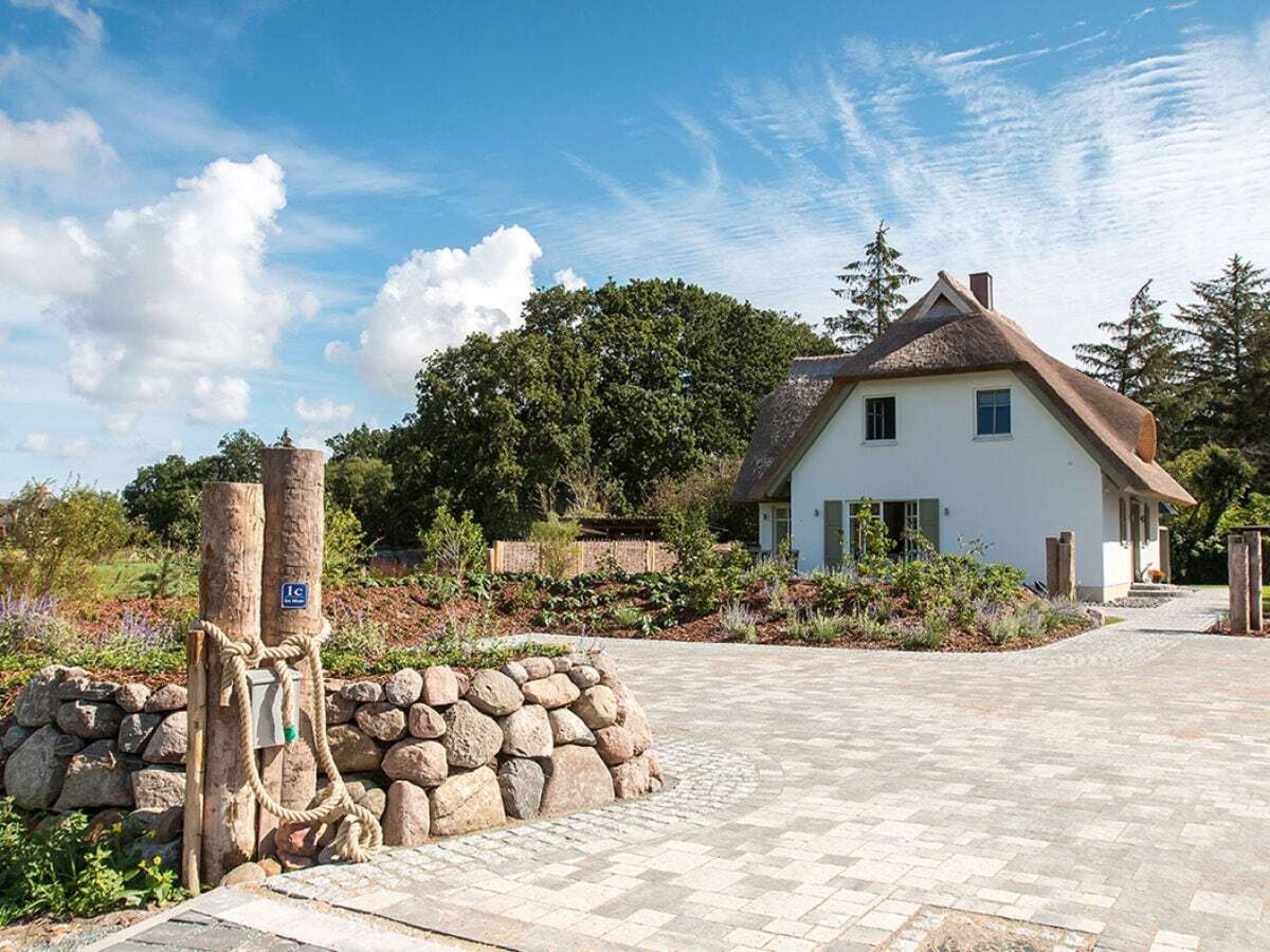 A white house with a thatched roof, a stone wall, and a paved driveway.