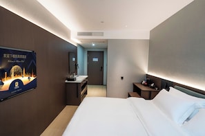 A hotel room with a bed, a desk, a mirror, and a TV mounted on the wall. - Caelum Gaudia Hotel (Guangzhou)