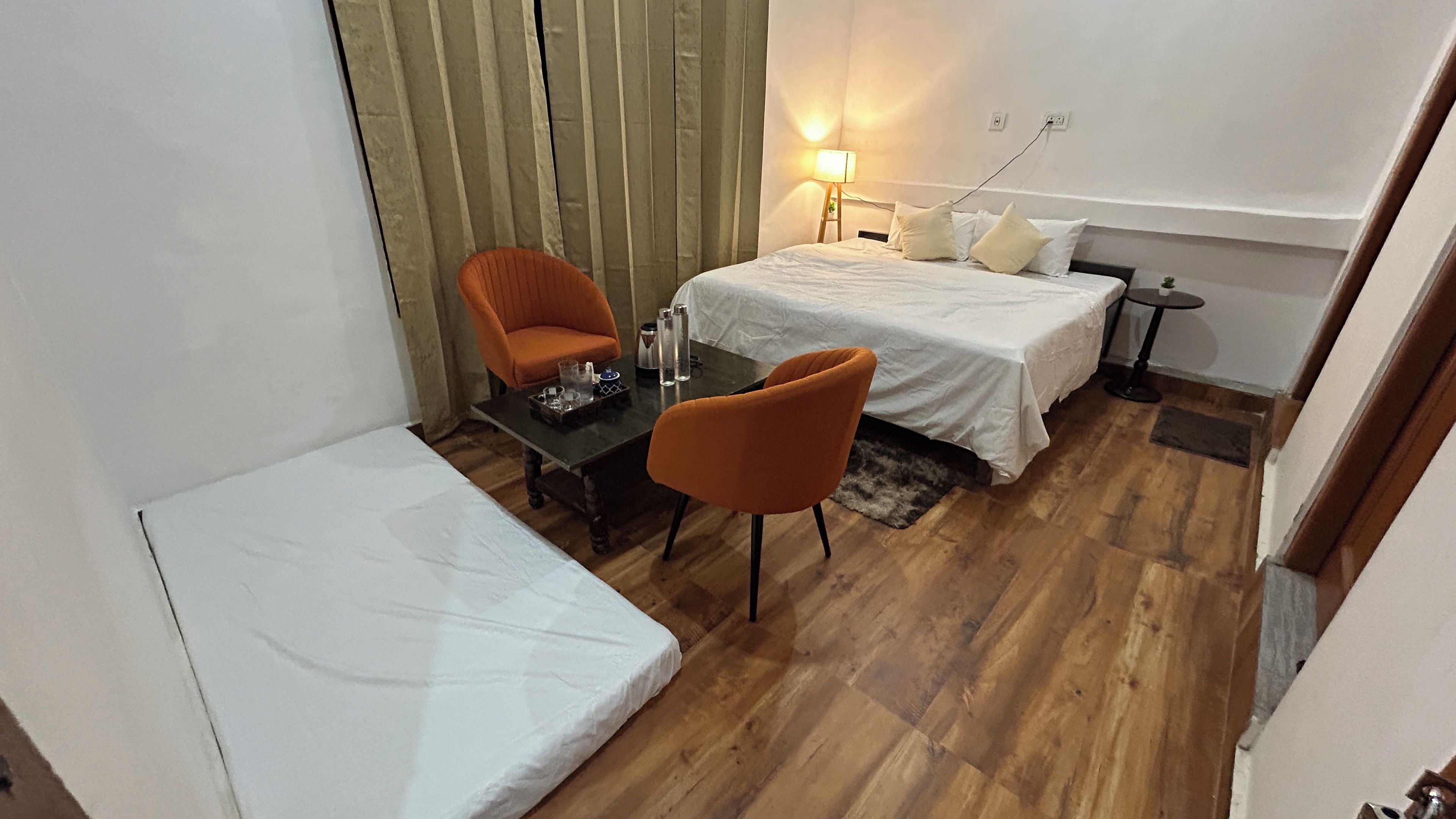A hotel room with a bed, two chairs, a small table, a lamp, and a nightstand.