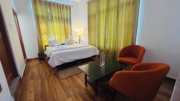 A hotel room with a bed, two pillows, a nightstand, a table with two bottles, and an orange chair.