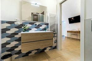 A modern bathroom with a geometric tile backsplash, a wooden vanity, a mirror, a towel rack, and a television on the wall. - Villa with pool, hot tub and annexe in Bisceglie (Bisceglie)