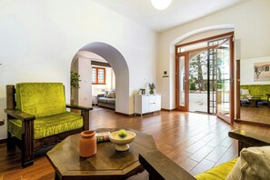 Un ampli saló amb una butaca verda, una taula de centre amb un vas i una vista a través d'una porta de vidre a una zona exterior.