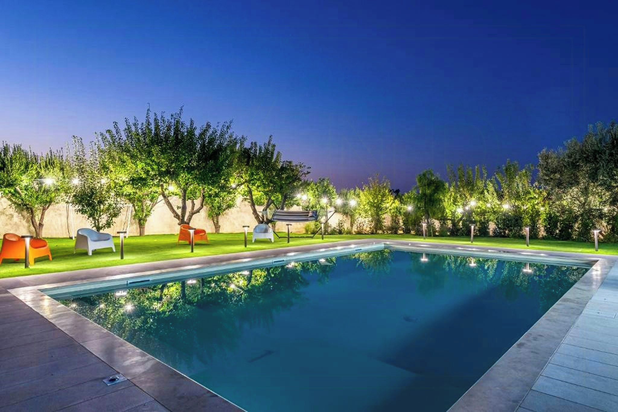 Una piscina con bordo lastricato, circondata da alberi e area relax all'aperto.