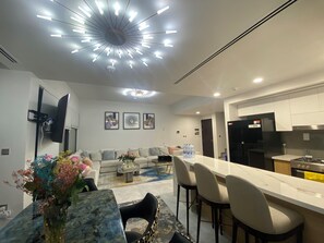 Eine moderne Küche mit einer zentralen Kochinsel, ein Essbereich mit Marmortisch und ein Wohnzimmer mit Sofa und Couchtisch.