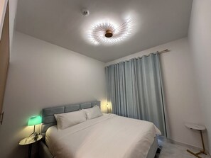 A modern hotel room with a bed, a nightstand with a lamp, a ceiling light fixture, and a window with curtains. - ⁠Cozy 3BR Townhouse Walk to Music Bars & Pet-Friendly Restaurants⁠ (Dubai)