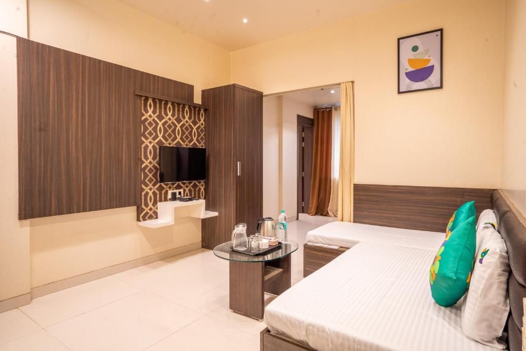 Une chambre d’hôtel avec un lit, une télévision, une petite table avec une bouilloire et une étagère fixée au mur.