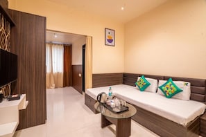 Habitación de hotel con sofá cama, mesa de centro de vidrio, televisión de pantalla plana y una obra de arte colgada en la pared.