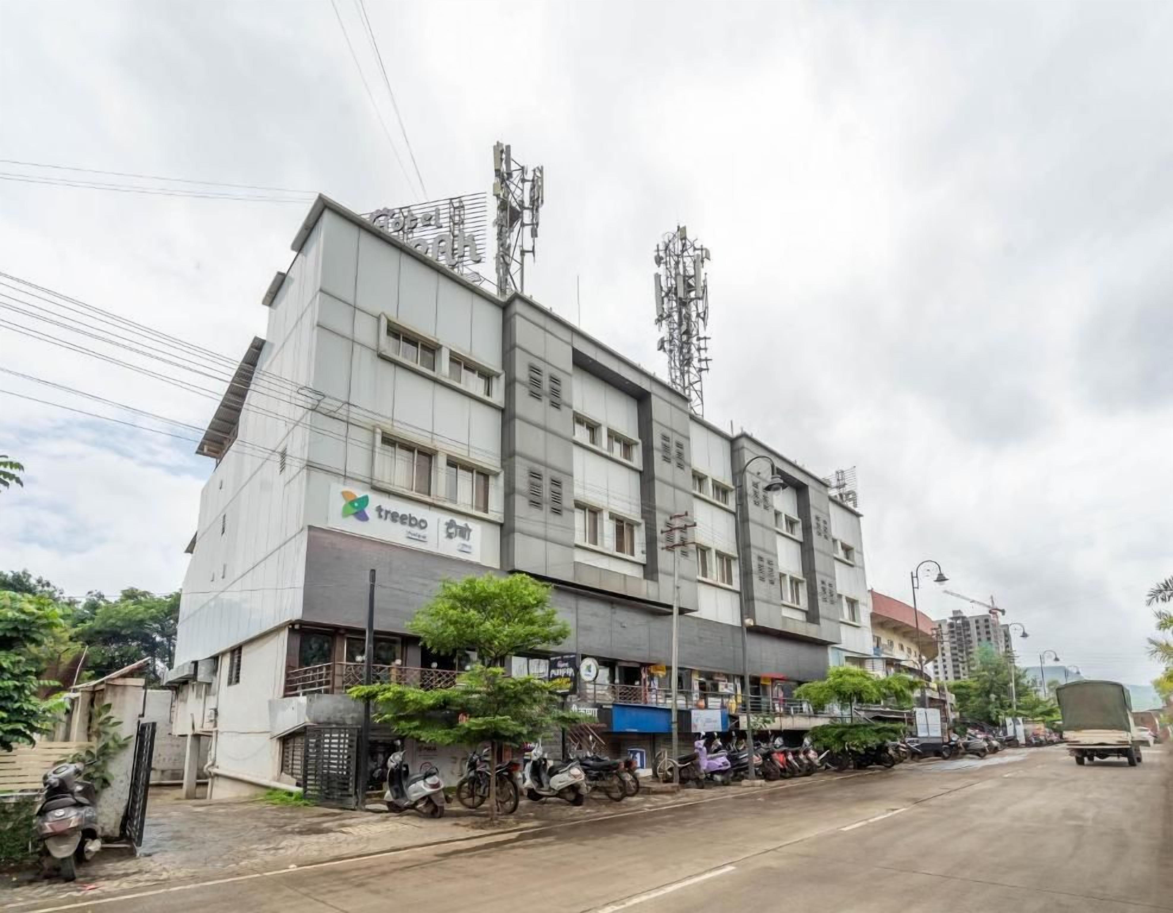 Un edificio de varios pisos con una planta baja comercial, un letrero que dice 'treebo' y varios vehículos estacionados.