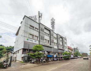 Un immeuble à plusieurs étages dont le rez-de-chaussée est occupé par des commerces, avec une enseigne indiquant « Treebo » et plusieurs véhicules stationnés à proximité.