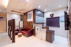Un espace d’accueil avec un canapé rouge, un comptoir de réception en bois et un panneau fixé au mur.
