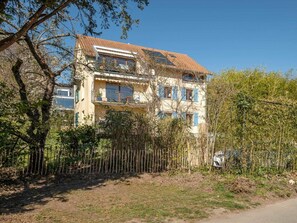 Ein mehrstöckiges Wohngebäude mit einem Ziegeldach, Balkonen und einer Zunruhe vor der Fassade.