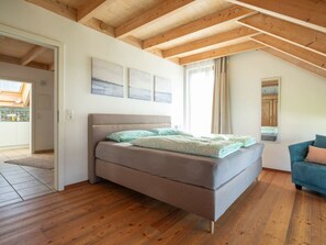Ein Schlafzimmer mit einem Bett, Holzboden, einer geneigten Decke und einem Fenster.