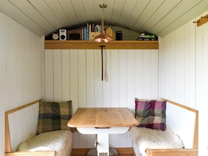 A cozy room with a wooden bench, a small table, and a shelf with various items. - Romney Hut - UKC4067 (West Bagborough, near Taunton)