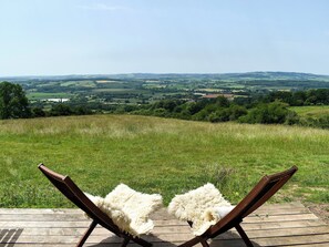 A wooden deck with two lounge chairs facing a grassy field and distant hills. - 0 bedroom accommodation in West Bagborough, near Taunton (West Bagborough, near Taunton)