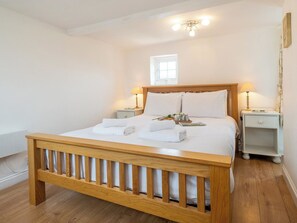 Ein ordentlich bezogenes Bett mit weißen Leinen und Handtüchern, ein hölzernes Kopfende, Nachttische mit Lampen, ein kleines Fenster und eine Heizung.