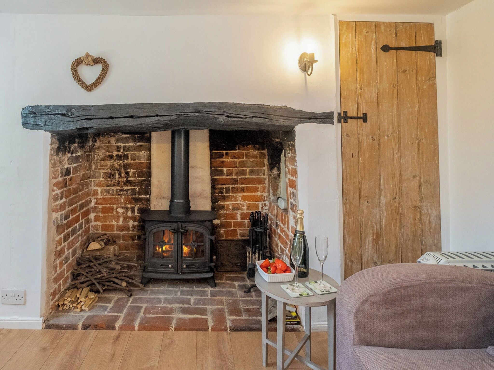 A cozy room with a brick fireplace, a wooden door, and a table with a bottle and glasses.
