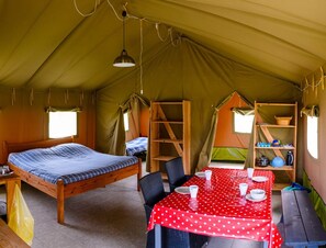 A tent with a bed, a dining table, and a shelf with items.