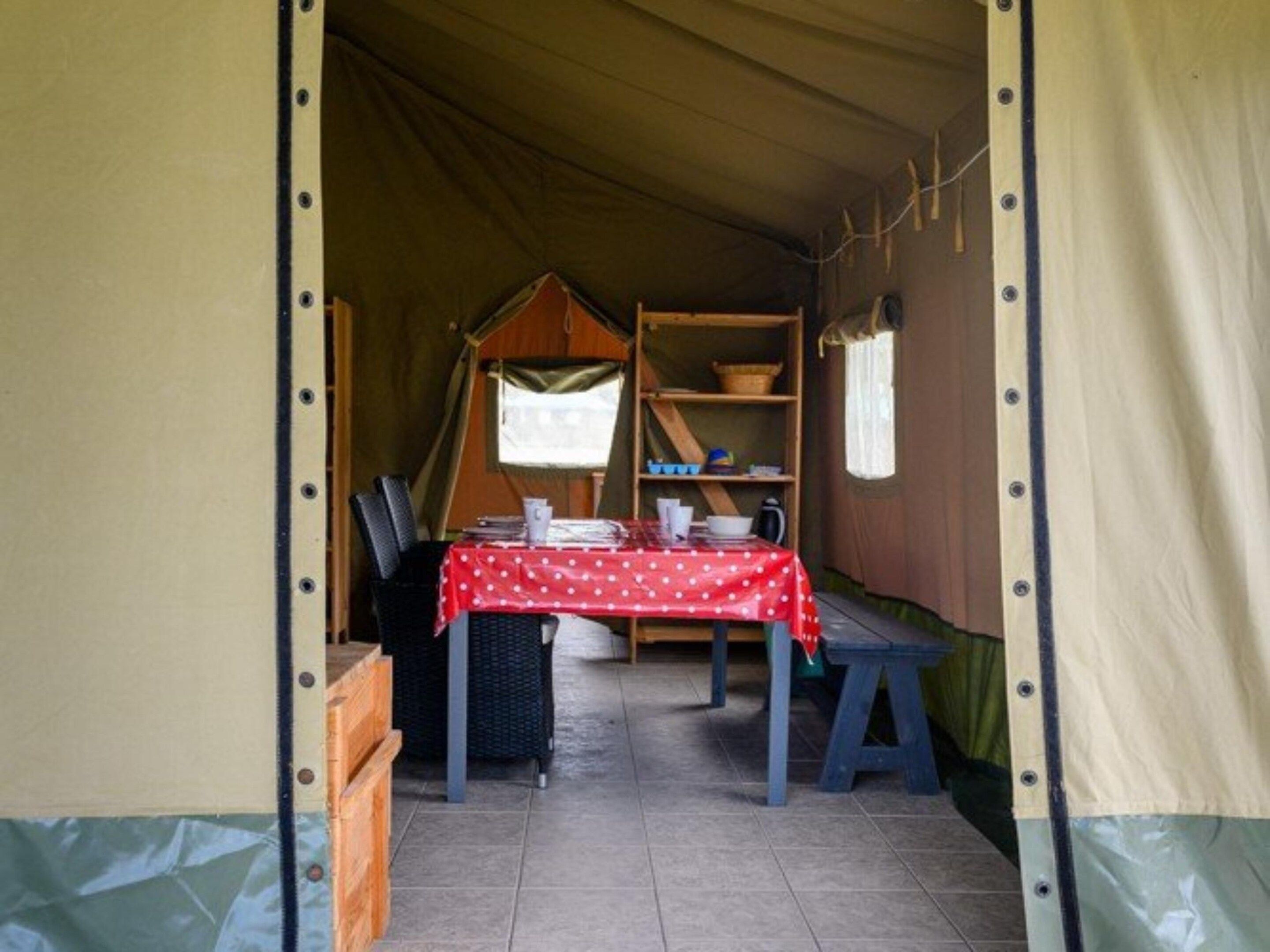 A tent with a table and chairs, a shelf with items, and a window.
