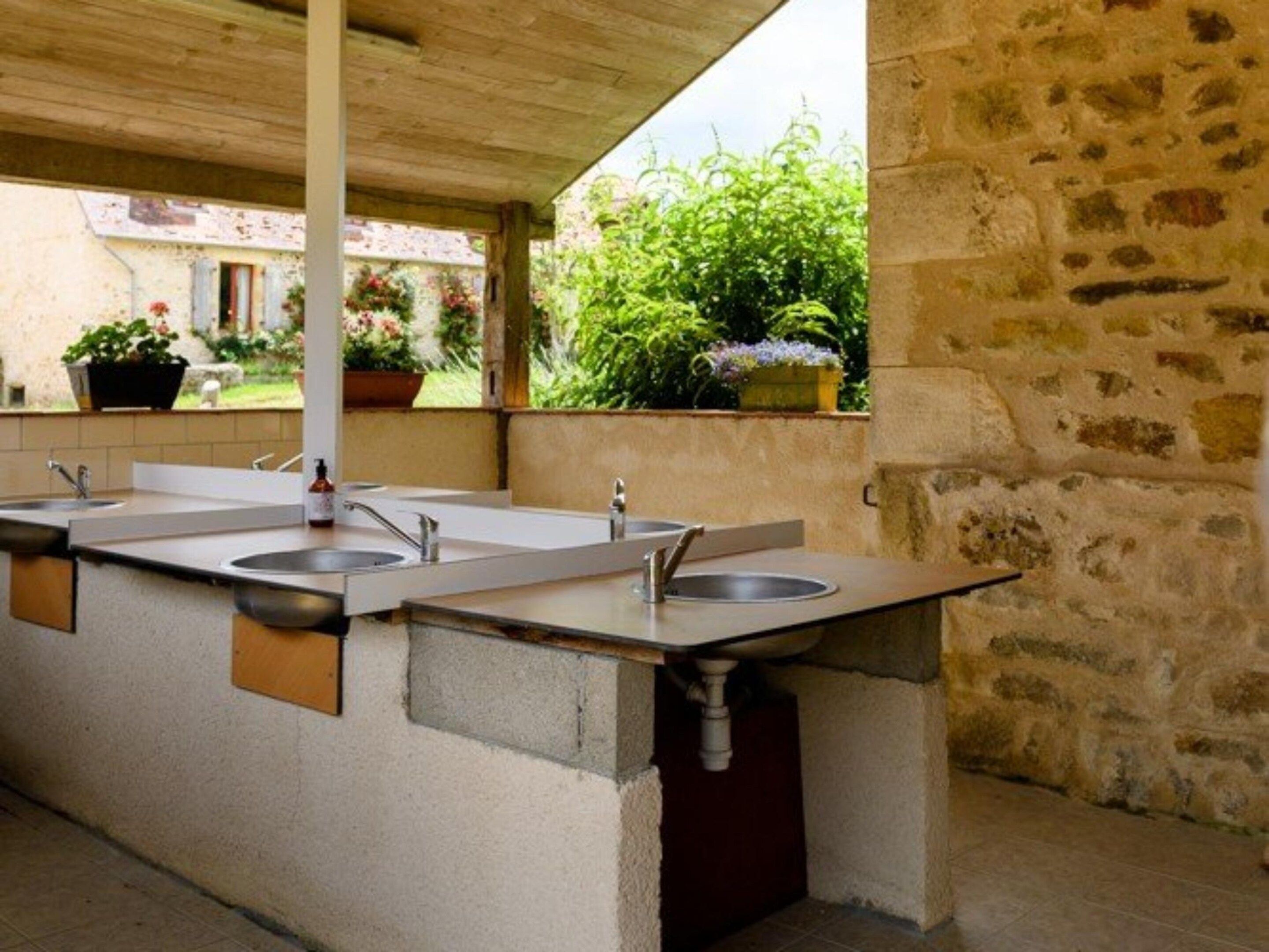 A covered outdoor area with a row of sinks and a stone wall.