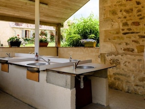 A covered outdoor area with a row of sinks and a stone wall.