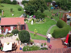 Ein gepflegter Garten mit Terrasse, einem kleinen Gebäude und verschiedenen Pflanzen und Blumen.